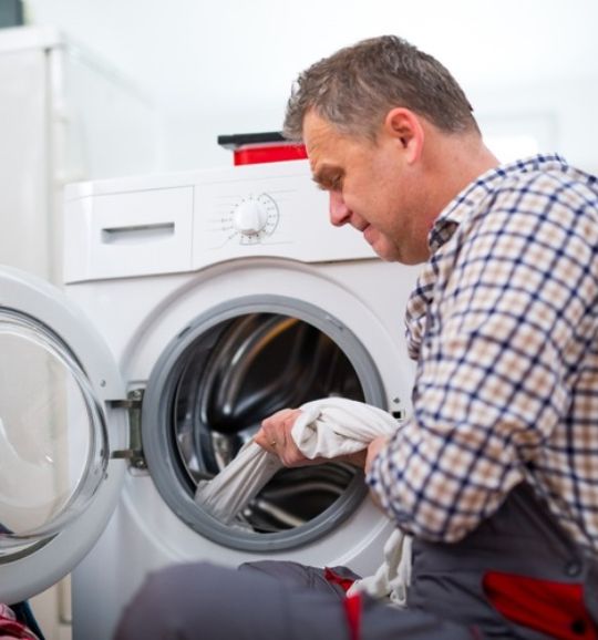 A man and woman sit near a washing machine, representing laundry appliance repair services available in San Antonio, TX.